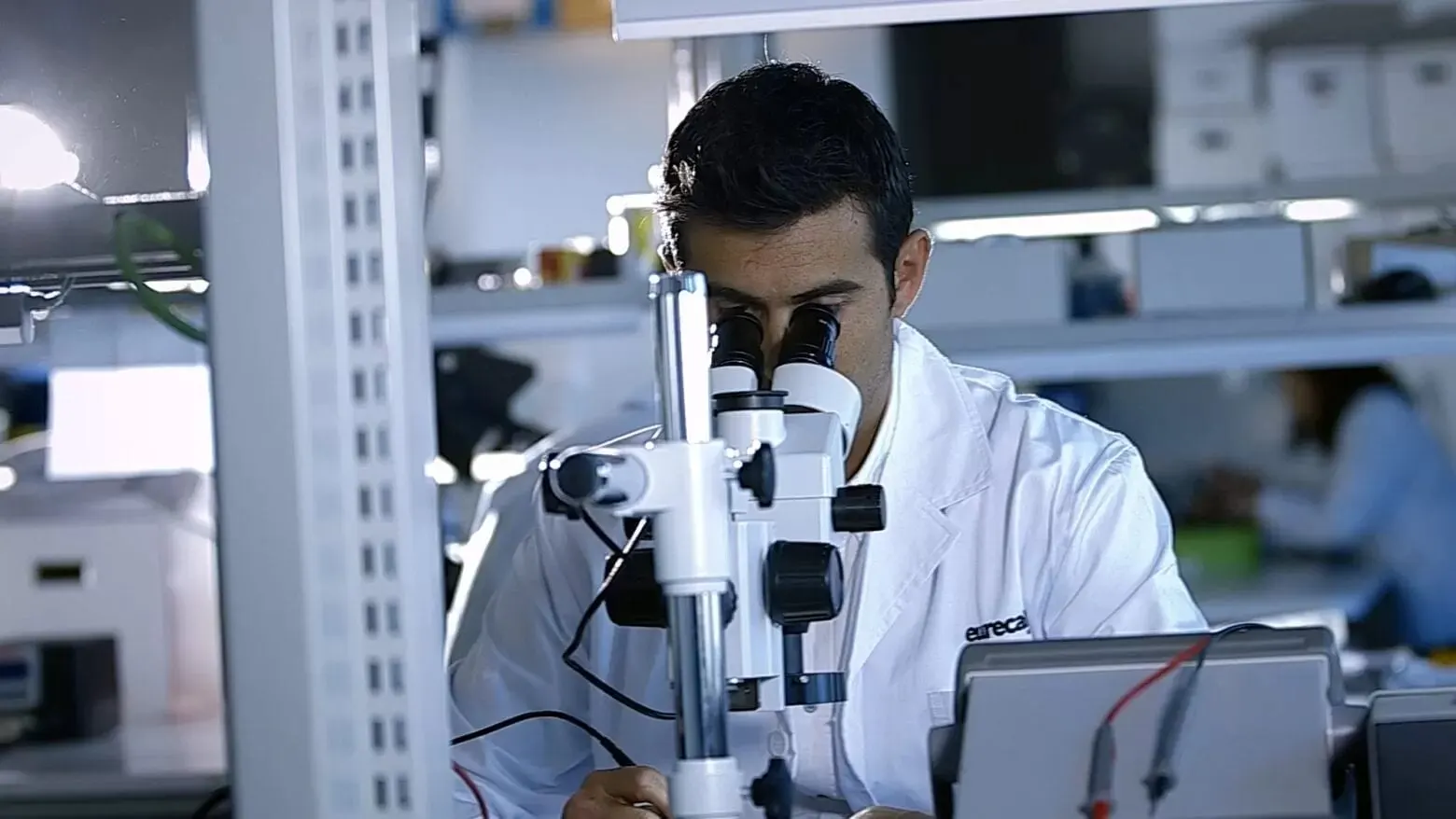 Investigador d'Eurecat amb bata blanca treballant amb un microscopi al laboratori